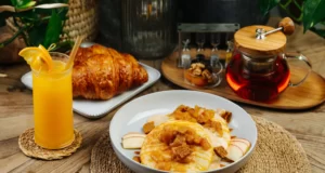 Fluffy pancakes topped with caramelized apples and crumble served with fresh croissant, apple slices, and hot tea.