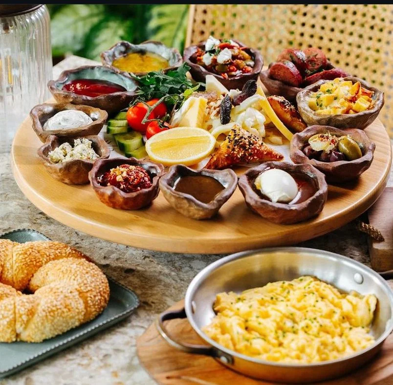 Traditional Turkish breakfast spread with eggs, olives, cheese, bread, pastries, and warm comfort dishes on a rustic table.