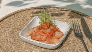 A plate of kimchi with garnishes on the top, with cutlery on the side