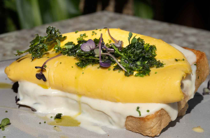 Cheesy Omelet: Omelet stuffed with goat cheese, kashkaval cheese, and bechamel sauce served on home-made sourdough bread and garnished with fried kale and sprinkled with gremolata.