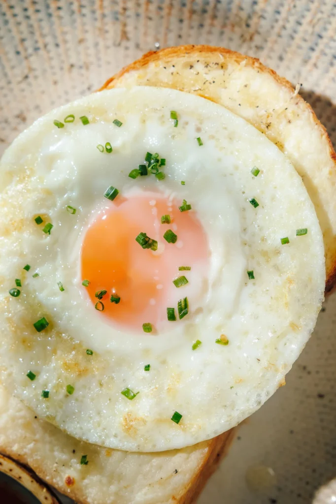 Close-up of a sunny-side-up egg on toasted bread, topped with chopped herbs, showcasing a simple and fresh breakfast dish