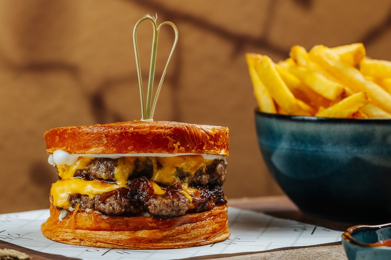 A delicious Cronut Burger at BohoX featuring a crispy, flaky cronut bun, juicy beef patties, melted cheese, caramelised onions, and a side of golden French fries