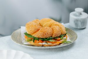 Smoked salmon bagel with sesame seeds, cream cheese, greens, pickled onion, and capers served on a ceramic plate