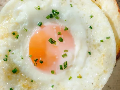 Close-up of a sunny-side-up egg on toasted bread, topped with chopped herbs, showcasing a simple and fresh breakfast dish