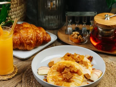 Fluffy pancakes topped with caramelized apples and crumble served with fresh croissant, apple slices, and hot tea.