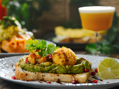 Avocado toast with fried cheese balls, garnished with cilantro and pomegranate seeds, served with lime and juice for a scenic breakfast in Business Bay