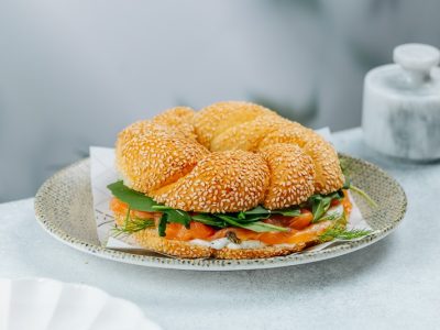Smoked salmon bagel with sesame seeds, cream cheese, greens, pickled onion, and capers served on a ceramic plate