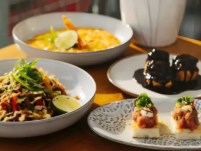 Brunch dishes with noodles, curry, desserts, and appetizers on a wooden table.