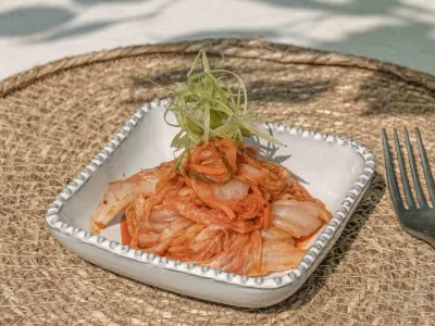 A plate of kimchi with garnishes on the top, with cutlery on the side