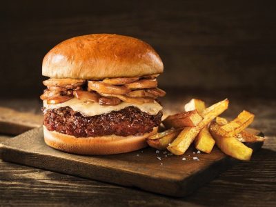 Wagyu beef burger served with crispy fries on a wooden plate.